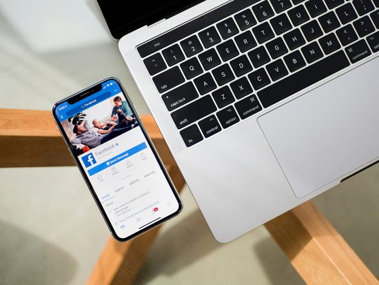Iphone mit Facebook geöffnet neben einem Macbook