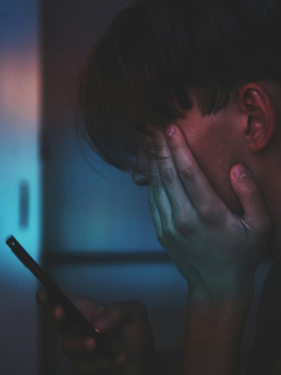 Ein verzweifelter Mensch mit kurzen Haaren, blickt auf ein Smartphone in seiner Hand