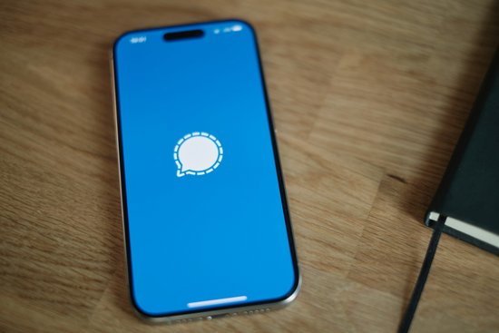 Ein Smartphone liegt auf einem Holztisch. Das blau-weiße Signal Logo wird angezeigt.