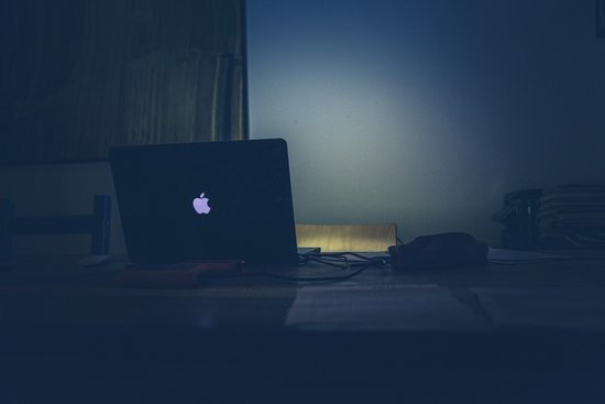 Laptop mit Apple Logo in dunklem Raum mit leuchtendem Bildschirm